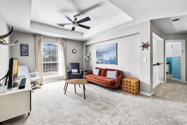 carpeted living area featuring a raised ceiling, a textured ceiling, baseboards, and a ceiling fan