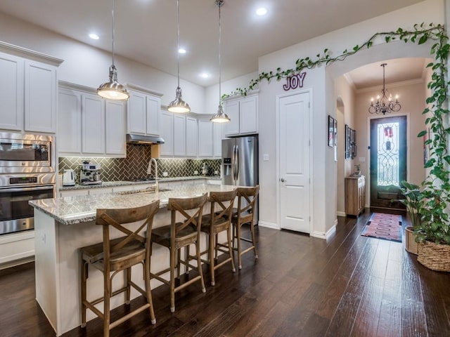 915 Enchanted Wood Dr, Arlington, TX 76005 - kitchen featuring light stone countertops, under cabinet range hood, arched walkways, stainless steel appliances, and tasteful backsplash