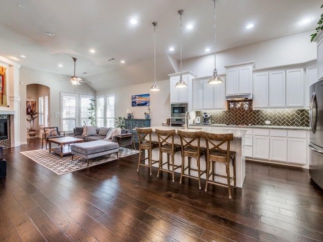 915 Enchanted Wood Dr, Arlington, TX 76005 - kitchen featuring a breakfast bar area, decorative backsplash, open floor plan, a ceiling fan, and a glass covered fireplace