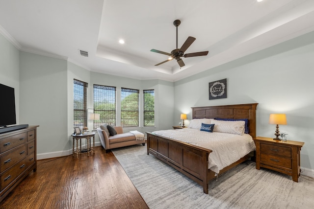 bedroom featuring a tray ceiling, wood finished floors, visible vents, ornamental molding, and baseboards