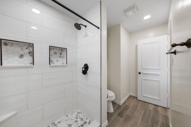 bathroom featuring toilet, a tile shower, baseboards, visible vents, and wood finish floors