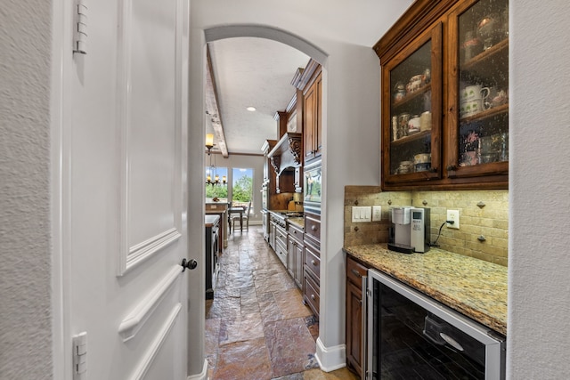 bar with stone tile flooring, arched walkways, tasteful backsplash, baseboards, and beverage cooler