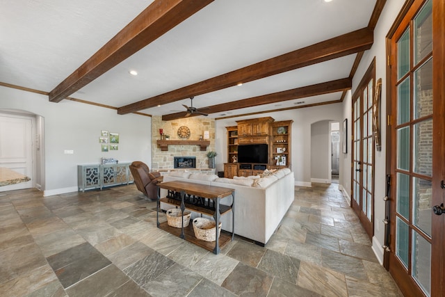 living area featuring ceiling fan, arched walkways, stone tile flooring, and baseboards