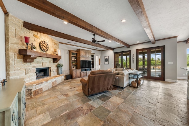 living room featuring stone tile flooring, baseboards, beamed ceiling, a ceiling fan, and a fireplace