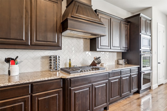 9724 Croswell St, Fort Worth, TX 76244 - kitchen with premium range hood, appliances with stainless steel finishes, backsplash, dark brown cabinets, and light wood-type flooring