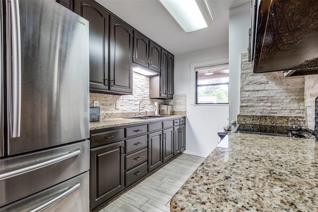 kitchen featuring a sink, light wood finished floors, backsplash, light stone countertops, and freestanding refrigerator