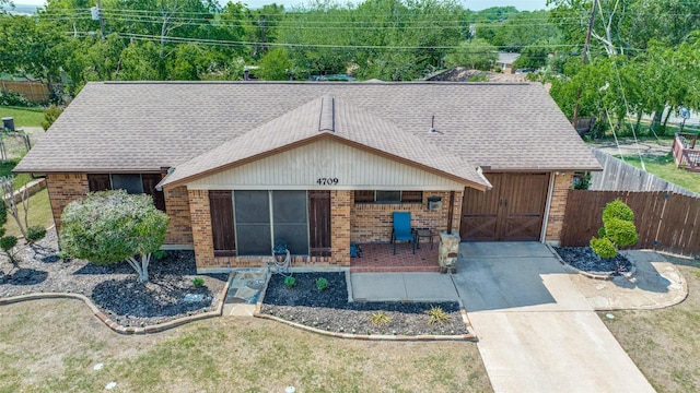view of front of property with fence, brick siding, roof with shingles, and concrete driveway