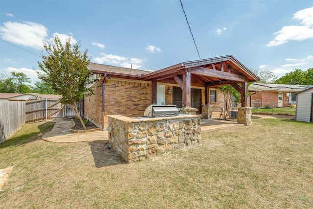 back of property with a fenced backyard, a yard, an outdoor kitchen, and a patio area