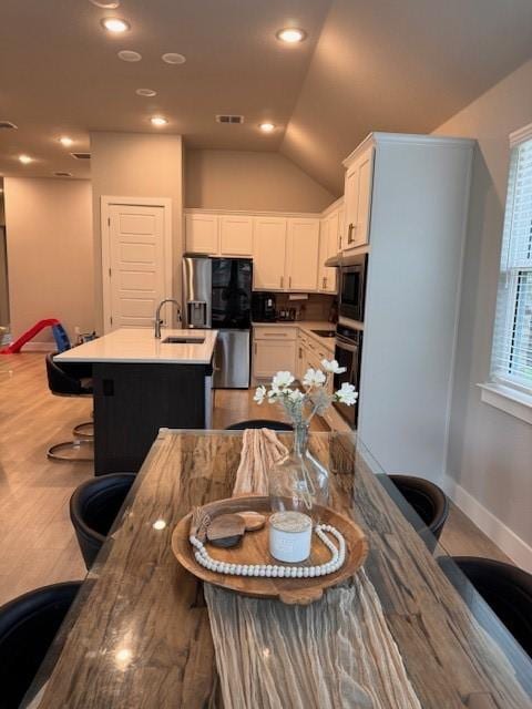 kitchen featuring oven, stainless steel fridge with ice dispenser, visible vents, a sink, and white cabinetry