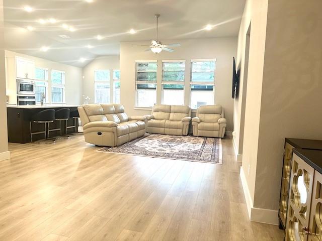 living area with light wood-style floors, vaulted ceiling, baseboards, and ceiling fan