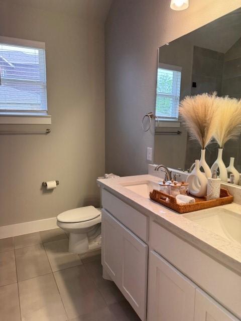 bathroom with tile patterned floors, a sink, double vanity, baseboards, and toilet
