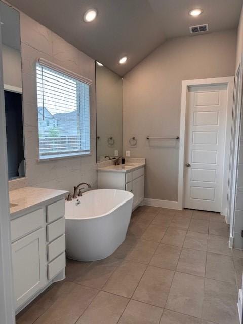 full bathroom with vaulted ceiling, a soaking tub, tile patterned flooring, two vanities, and visible vents