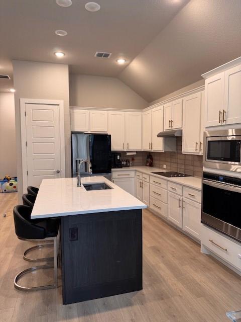 kitchen with a sink, vaulted ceiling, visible vents, under cabinet range hood, and appliances with stainless steel finishes