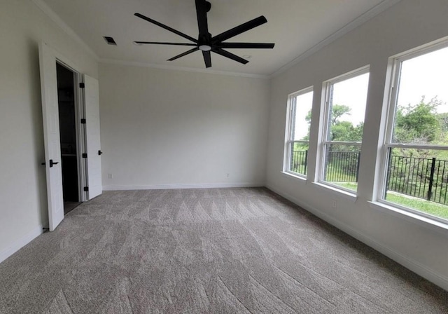 carpeted spare room featuring visible vents, baseboards, crown molding, and a ceiling fan