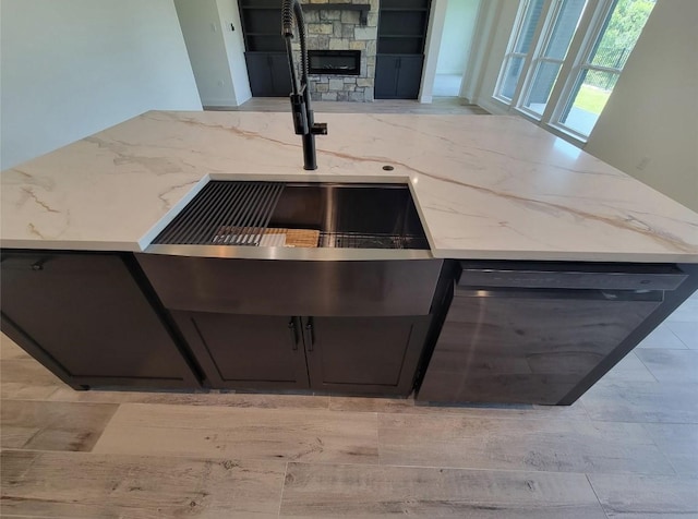 details with a sink, a stone fireplace, light wood-style floors, and light stone countertops