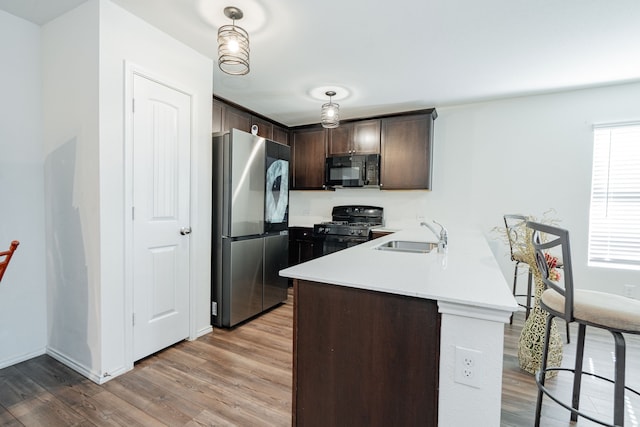 kitchen with a peninsula, dark brown cabinets, black appliances, wood finished floors, and a sink
