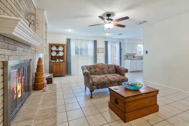 living area featuring a fireplace, light tile patterned floors, a textured ceiling, a ceiling fan, and visible vents