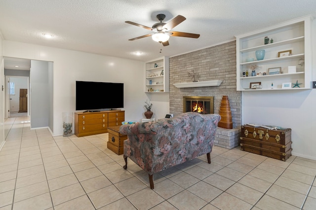 living area featuring a fireplace, a textured ceiling, a ceiling fan, light tile patterned flooring, and built in shelves