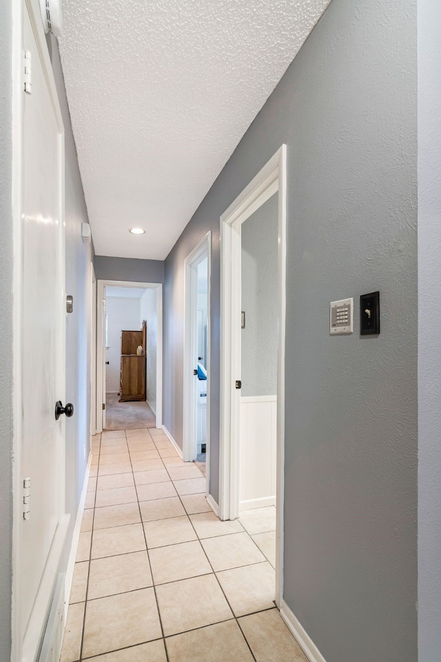 hall featuring light tile patterned floors, a textured ceiling, and baseboards