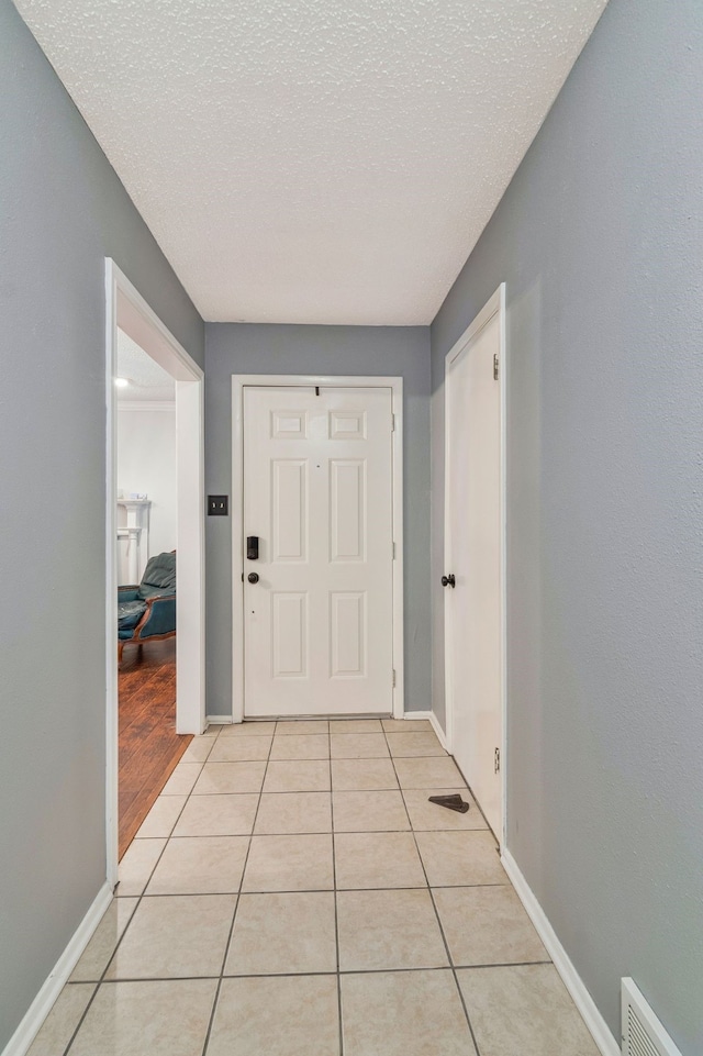 doorway to outside featuring a textured ceiling, light tile patterned flooring, baseboards, and visible vents