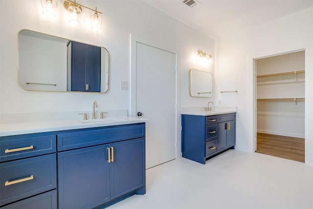 full bath featuring visible vents, a sink, a walk in closet, and two vanities