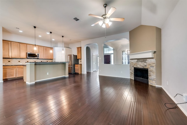 unfurnished living room with dark wood-style floors, visible vents, lofted ceiling, arched walkways, and ceiling fan