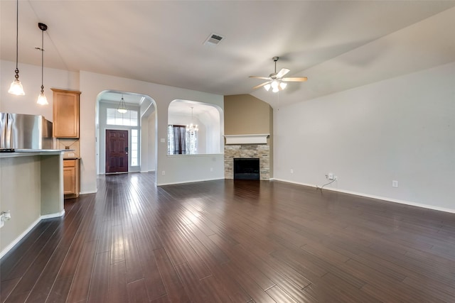 unfurnished living room featuring ceiling fan with notable chandelier, dark wood finished floors, arched walkways, vaulted ceiling, and baseboards
