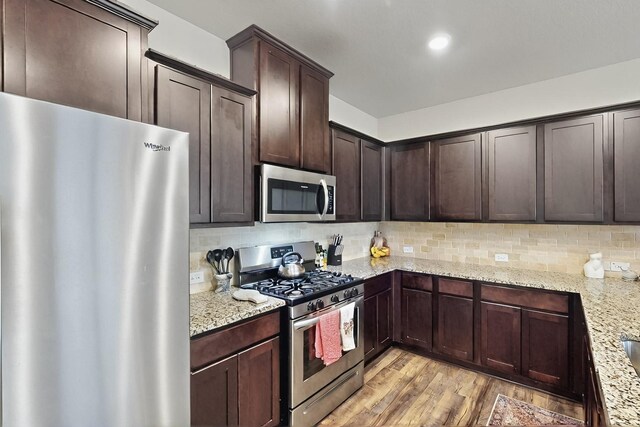 kitchen featuring appliances with stainless steel finishes, light wood-type flooring, dark brown cabinets, decorative backsplash, and light stone countertops