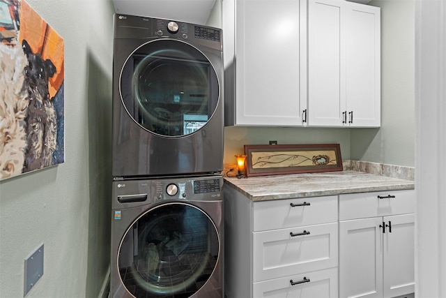 clothes washing area featuring stacked washer / drying machine and cabinet space