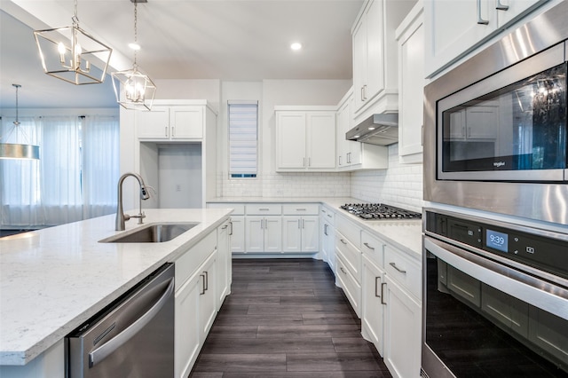 kitchen featuring white cabinets, an inviting chandelier, wall chimney exhaust hood, a sink, and appliances with stainless steel finishes