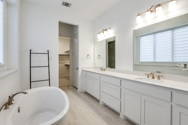 full bath featuring a freestanding bath, double vanity, a sink, and visible vents