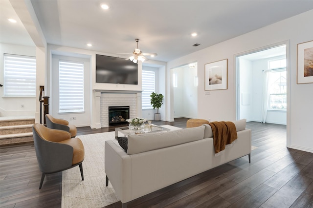 living room featuring dark wood-type flooring, a fireplace, a ceiling fan, and visible vents