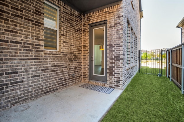 view of exterior entry featuring a patio area, a lawn, fence, brick siding, and a gate