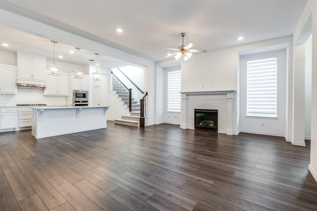 unfurnished living room with ceiling fan, recessed lighting, stairway, a brick fireplace, and dark wood-style floors