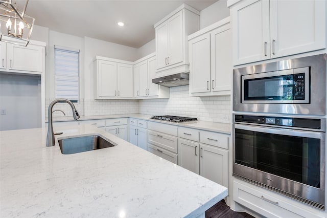 kitchen featuring under cabinet range hood, tasteful backsplash, a sink, and appliances with stainless steel finishes