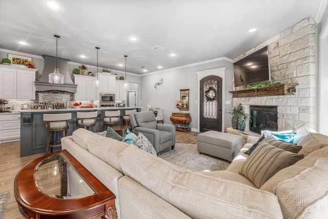 living area featuring a fireplace, light wood-style flooring, ornamental molding, visible vents, and recessed lighting