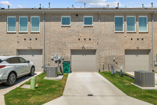 rear view of property featuring cooling unit, driveway, a garage, and brick siding