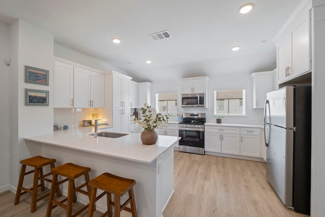 kitchen featuring visible vents, a sink, a peninsula, stainless steel appliances, and light wood-style flooring