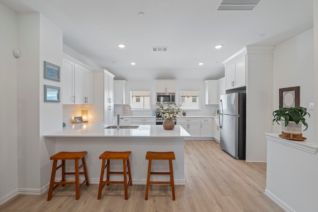 kitchen with visible vents, a sink, appliances with stainless steel finishes, a peninsula, and decorative backsplash
