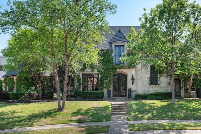 french country home with roof with shingles, french doors, and a front yard