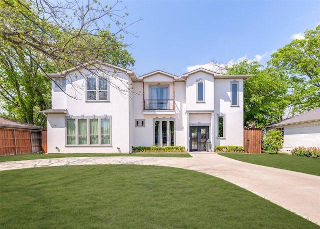view of front facade featuring stucco siding, a front yard, fence, a balcony, and french doors