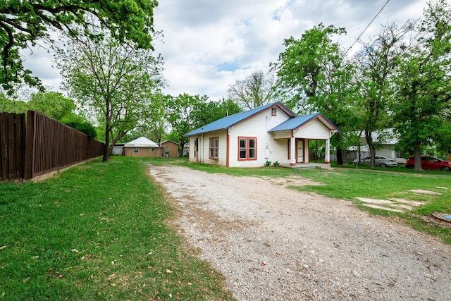 view of front of house with a front yard, metal roof, fence, and dirt driveway
