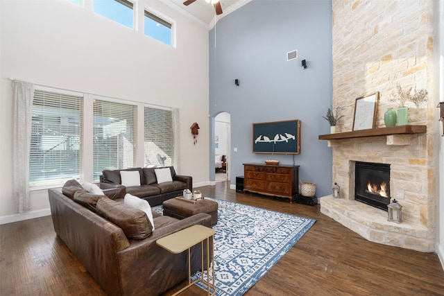 living area with a high ceiling, wood finished floors, a stone fireplace, a ceiling fan, and ornamental molding