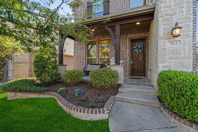 view of exterior entry with brick siding and a porch