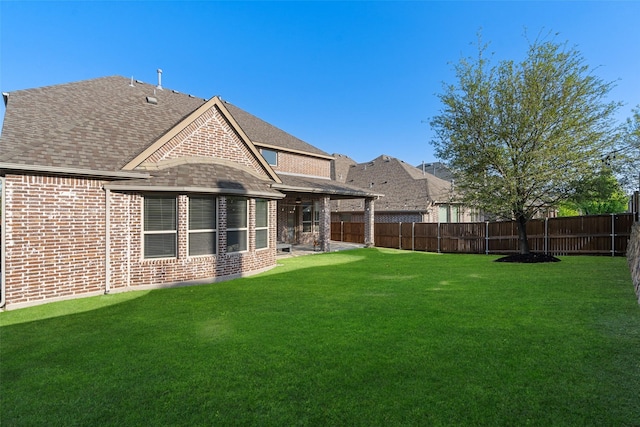 back of property featuring a fenced backyard, brick siding, a yard, and roof with shingles