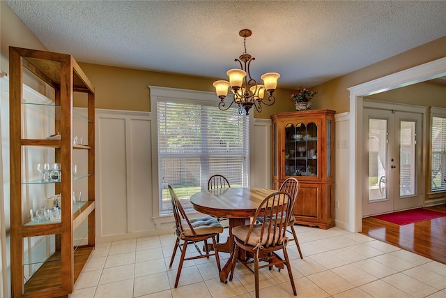 dining area with a decorative wall, a textured ceiling, a chandelier, light tile patterned flooring, and french doors