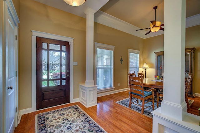 foyer featuring crown molding, ornate columns, a ceiling fan, wood finished floors, and baseboards