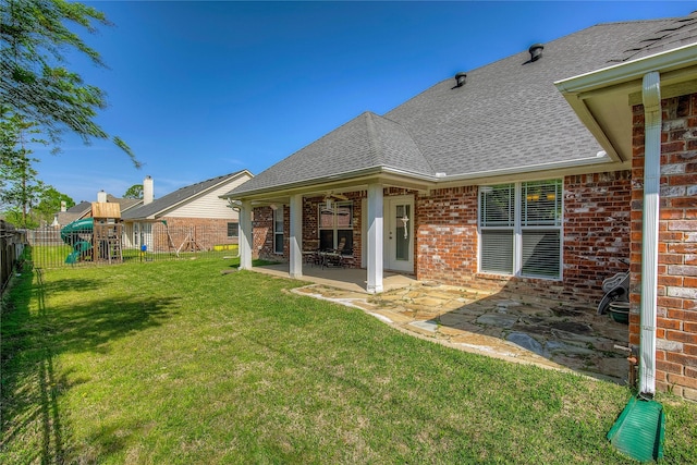 back of house featuring a patio area, a lawn, fence, a playground, and brick siding