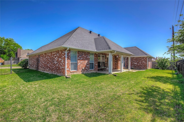 back of house with a shingled roof, a yard, a fenced backyard, a patio, and brick siding