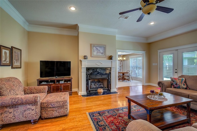 living room featuring french doors, crown molding, light wood-style floors, ceiling fan, and a premium fireplace